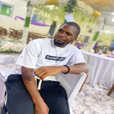 Young man sitting at event, casual attire, indoor setting.